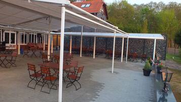 An outdoor patio area with tables and chairs, a covered seating area, and a stone wall in the background.