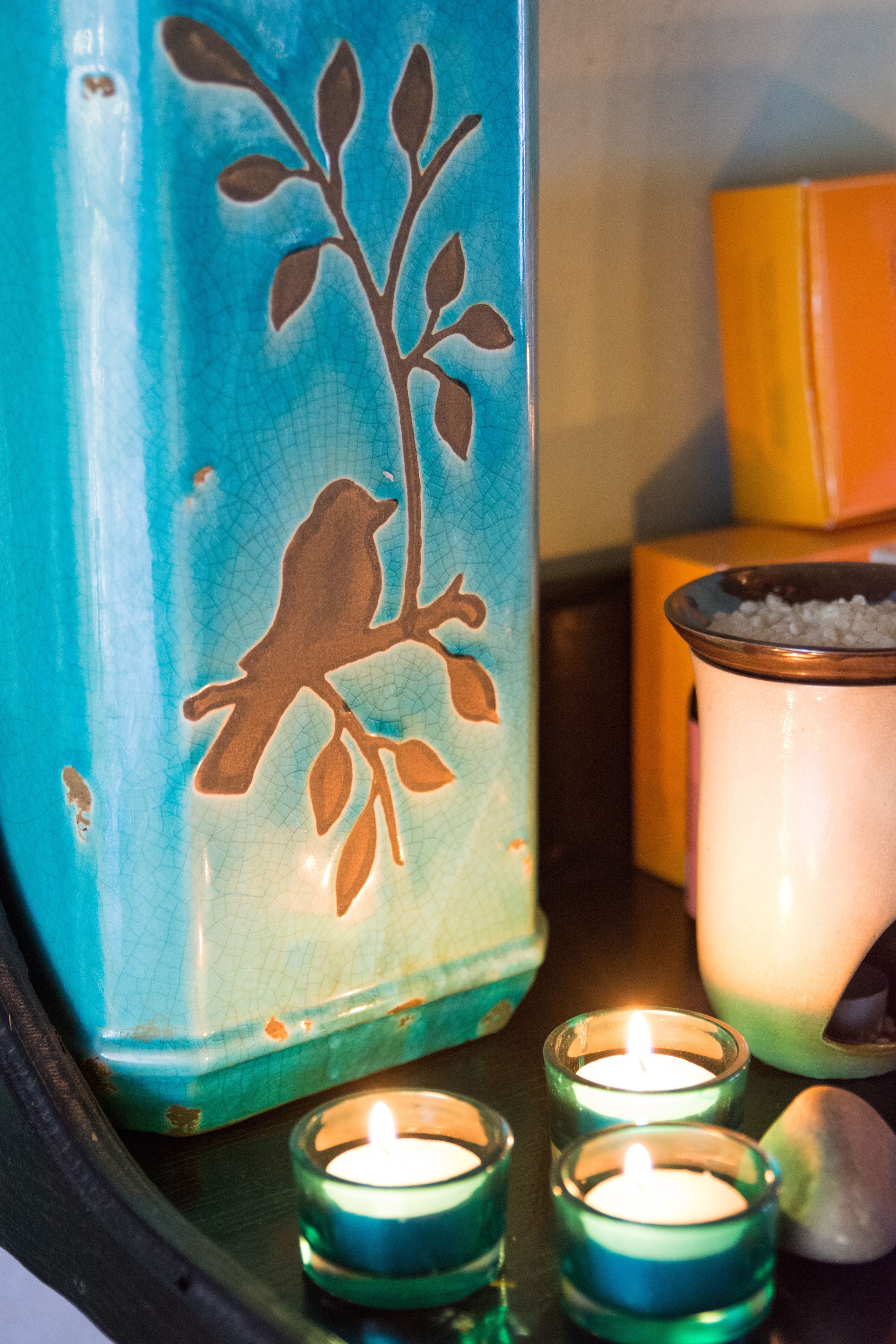 A teal ceramic vase with a bird design, a lit candle in a glass holder, and a salt shaker.