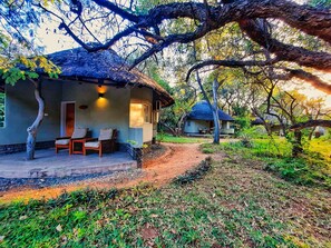 A rustic house with a thatched roof, a porch with chairs, and a dirt path leading to another building. - Sefapane Lodges and Safaris (Phalaborwa)