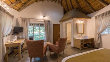 Experience a cozy retreat with a thatched roof ceiling, comfortable bed, and large window offering a view of the outdoors.