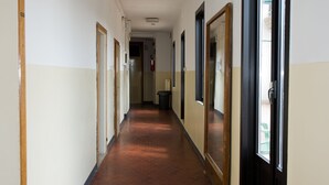 A long, narrow hallway with hexagonal patterned flooring, doors on both sides, and a fire extinguisher mounted on the wall. - Ostello Domus Civica (Venice)