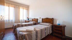 A hotel room with two beds, a wooden dresser, a nightstand, and a window with curtains. - Ostello Domus Civica (Venice)