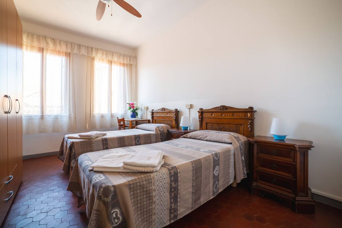 A hotel room with two beds, a wooden dresser, a nightstand, and a window with curtains.