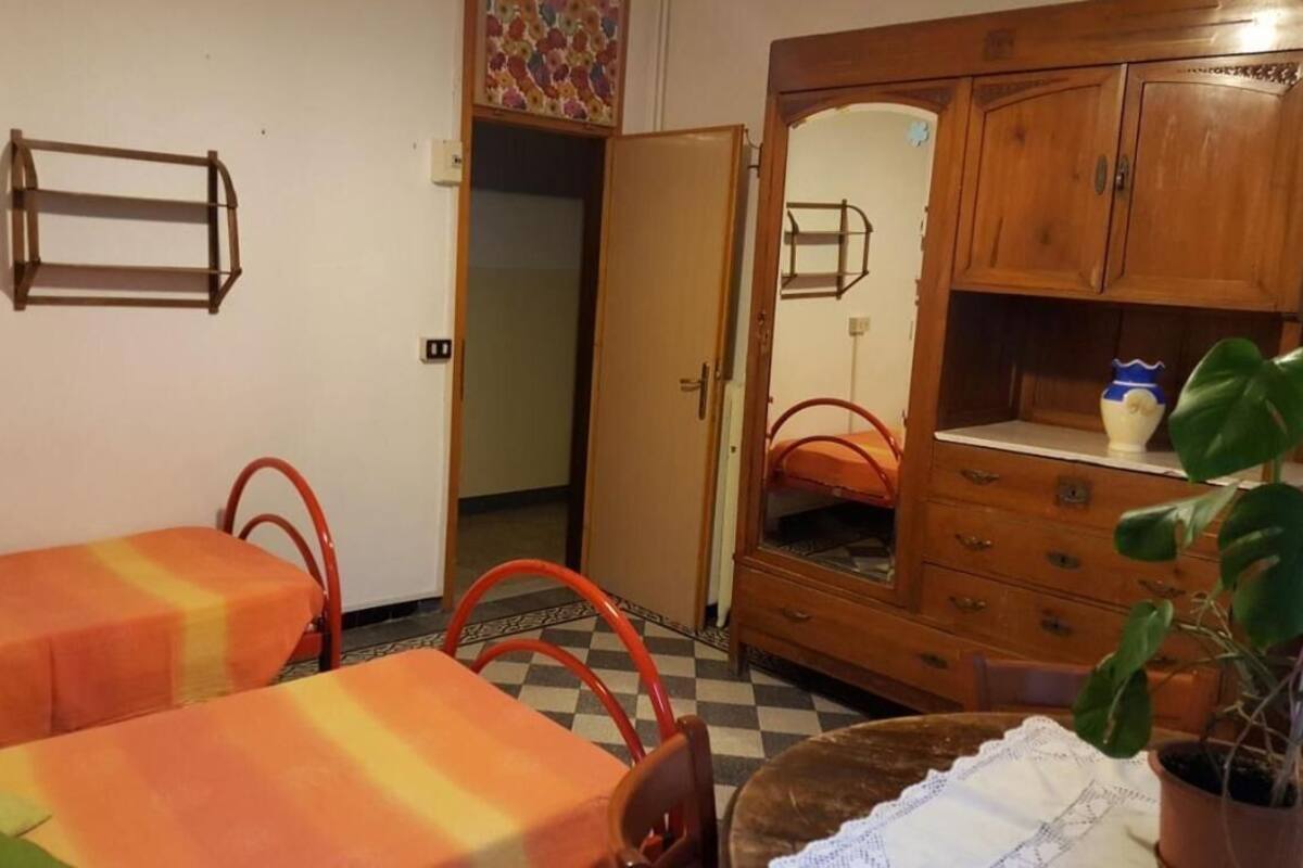 A room with two single beds, a wooden wardrobe, a mirror, a small table, and a potted plant.