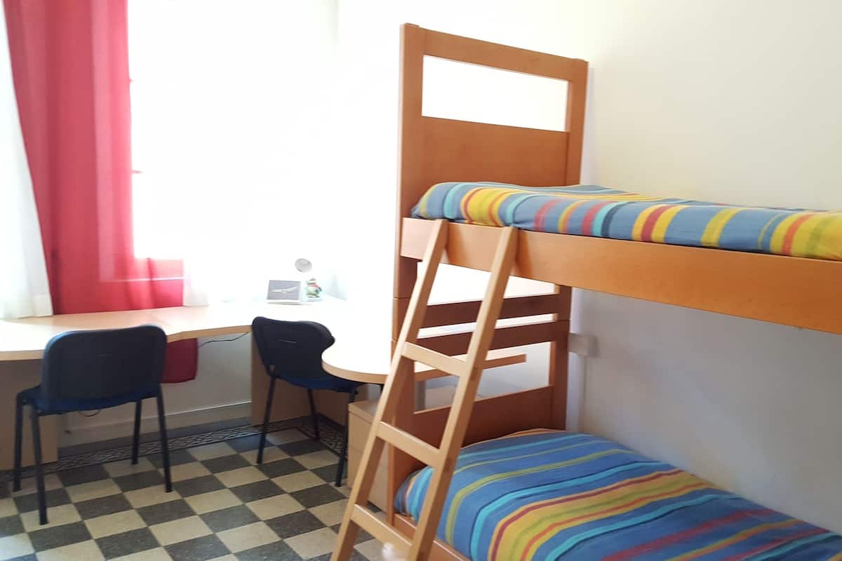 A bunk bed with a desk and chair, a window with red curtains, and a checkered floor.