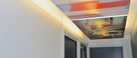 Un interior moderno con un diseño geométrico en el techo, una puerta visible con el número 19 y una pared con textura.