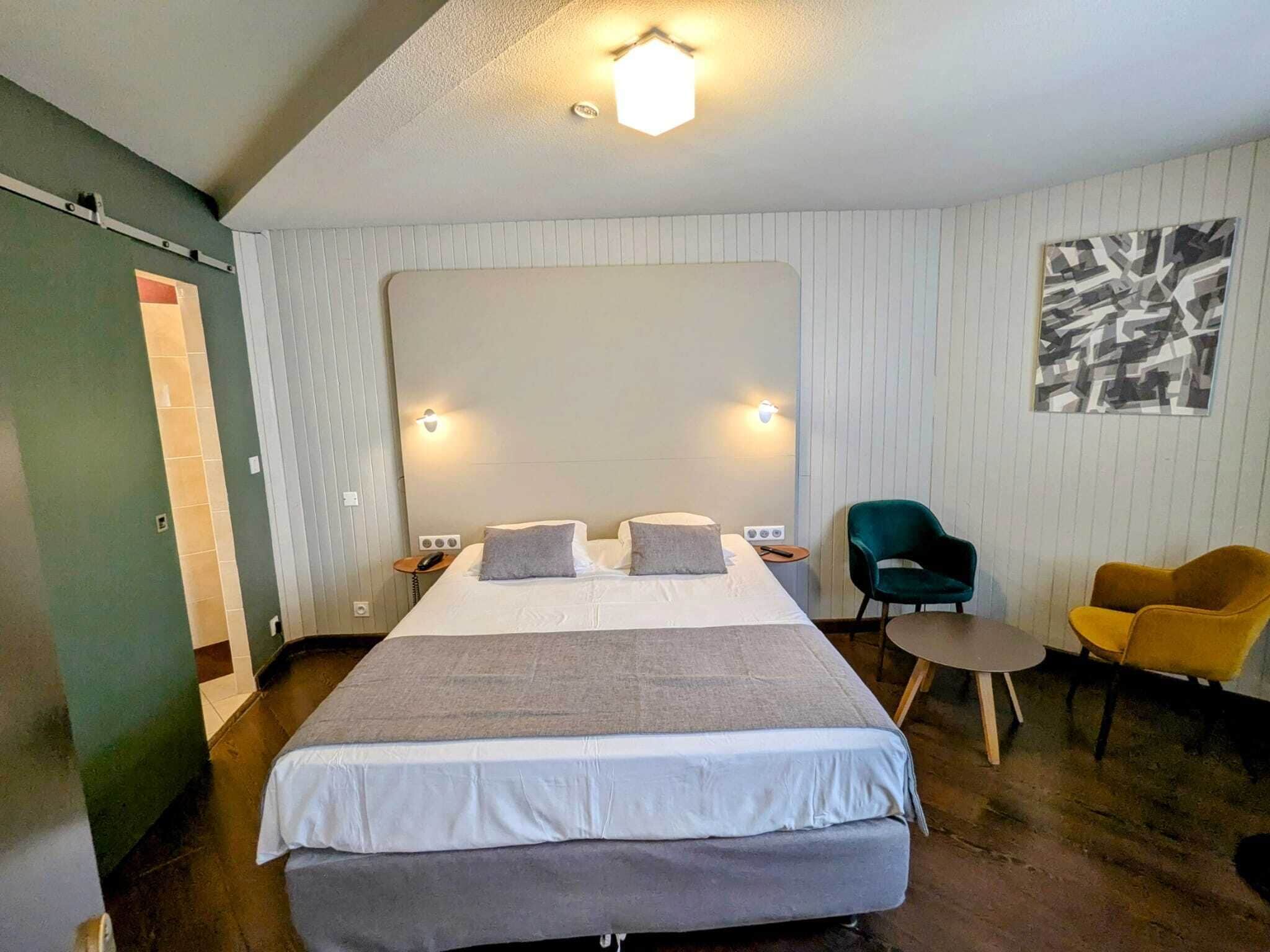 A hotel room with a large bed, two bedside tables, a desk, two chairs, and a wall-mounted light fixture.