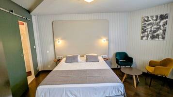 A hotel room with a large bed, two bedside tables, a desk, two chairs, and a wall-mounted light fixture.