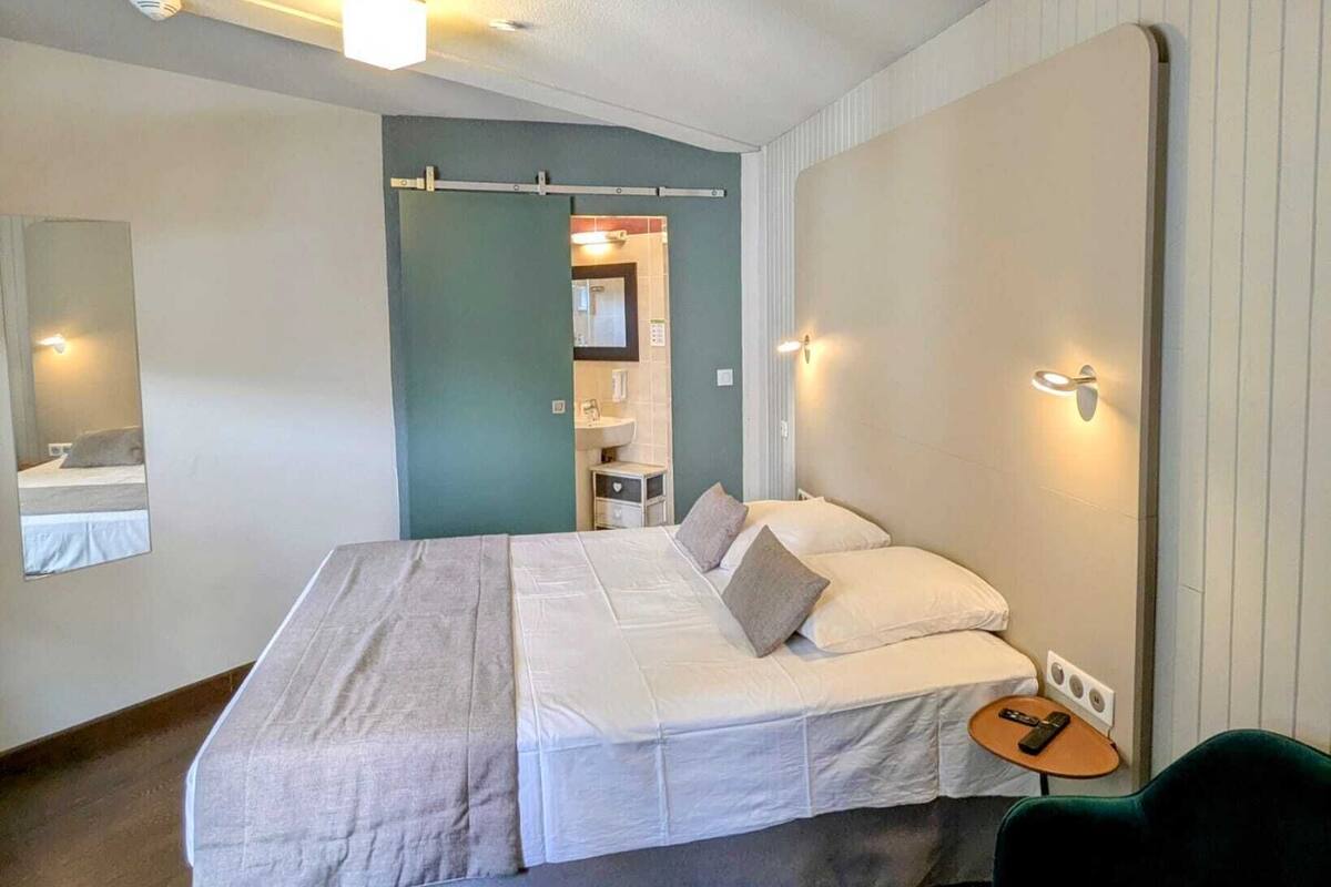 A bedroom with a bed, a bedside table, a chair, and a mirror.