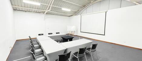 A conference room with a long table, chairs, a whiteboard, and a projector screen.