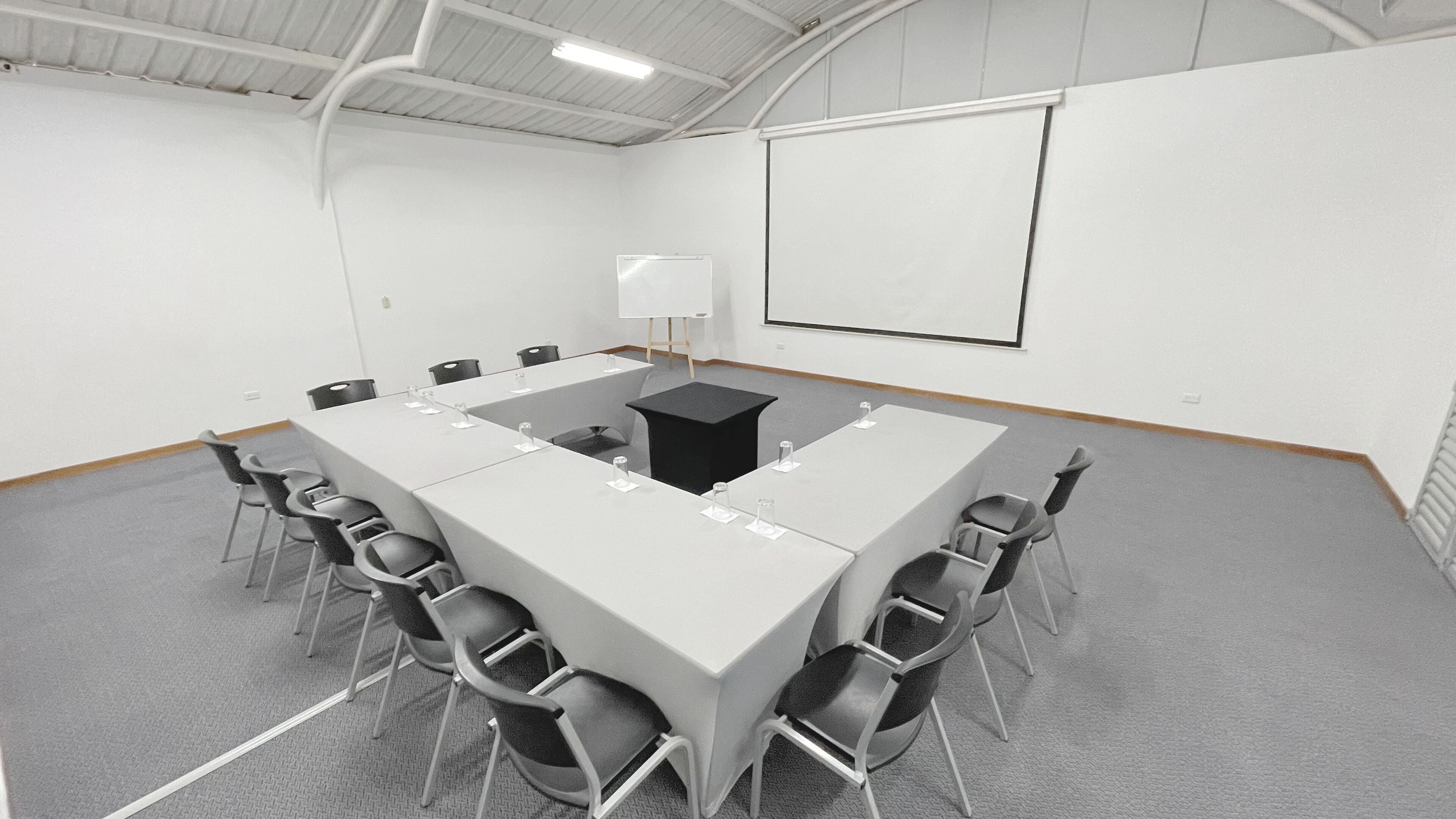 A conference room with a long table, chairs, a projector screen, and a whiteboard.