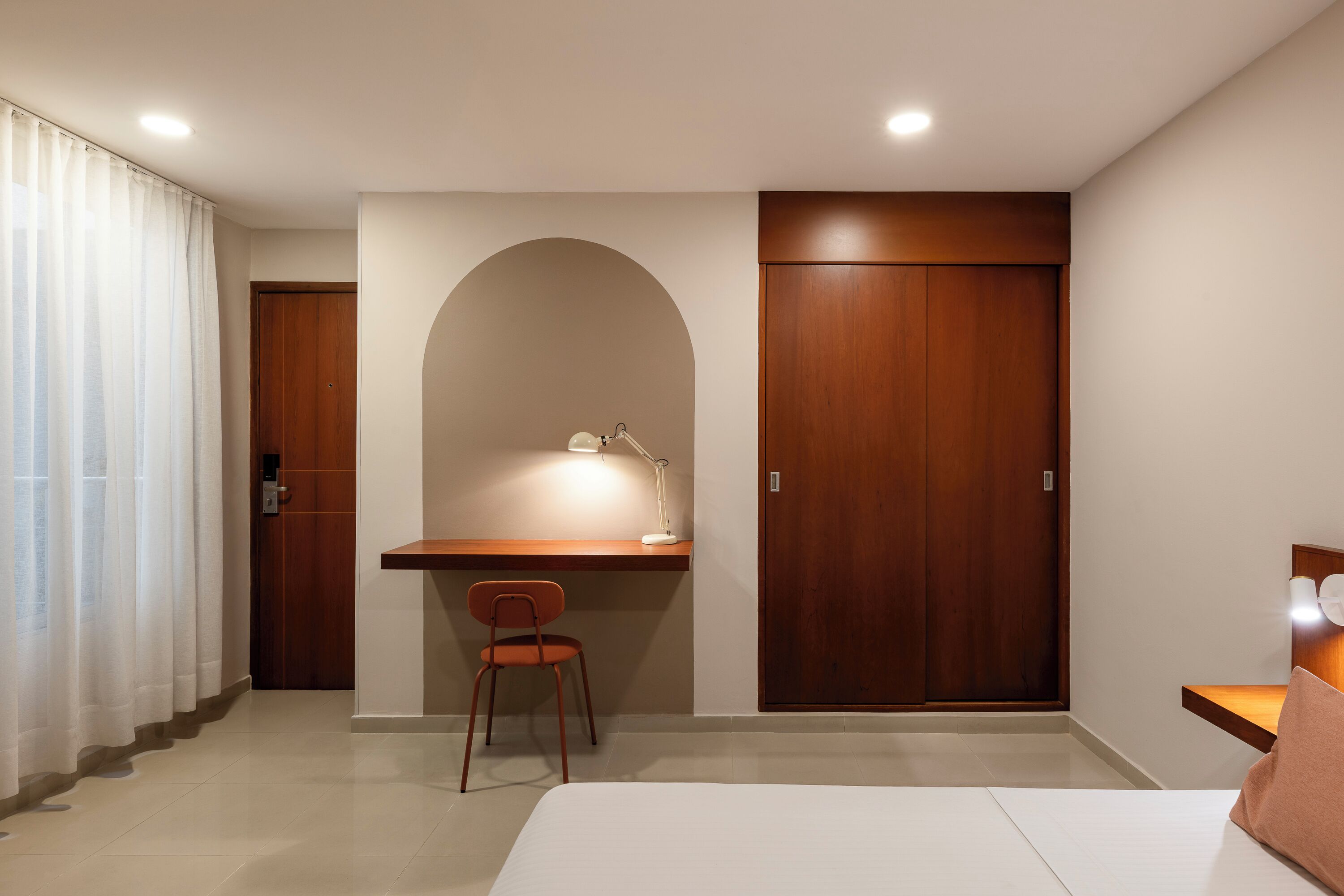 Hotelkamer met een bed, bureau met stoel, kast en deur naar de badkamer.