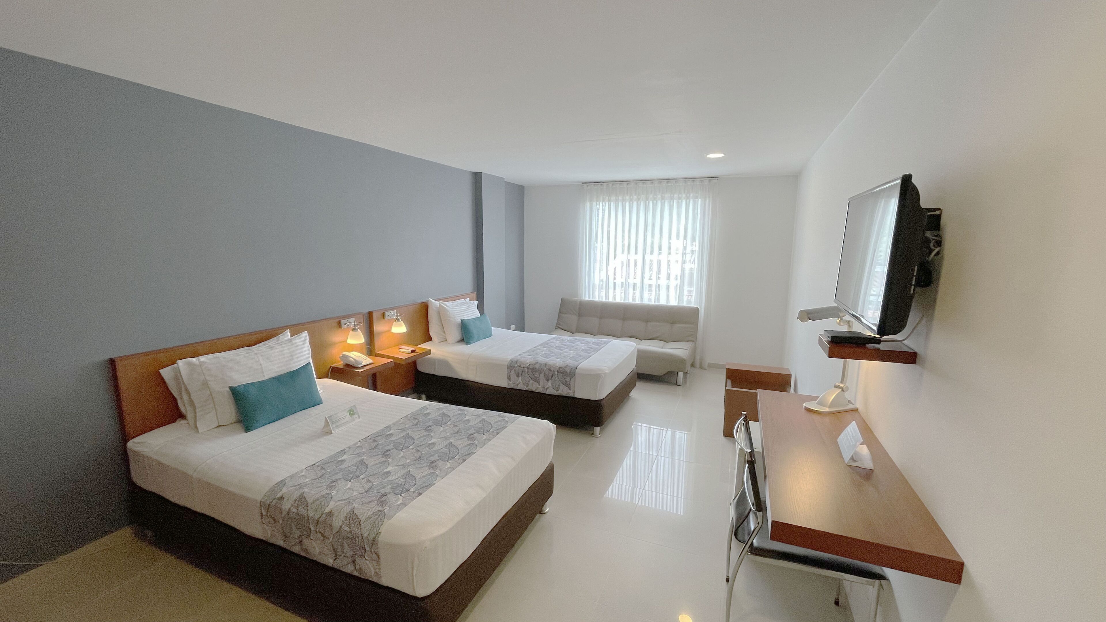 Habitación de hotel con dos camas, un sofá, un escritorio, un televisor y una ventana con cortinas.