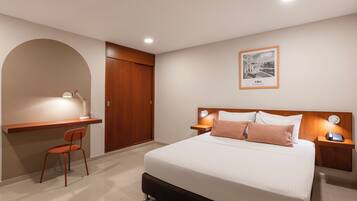 A hotel room with a bed, bedside tables, a desk with a chair, a wardrobe, and a framed picture on the wall.