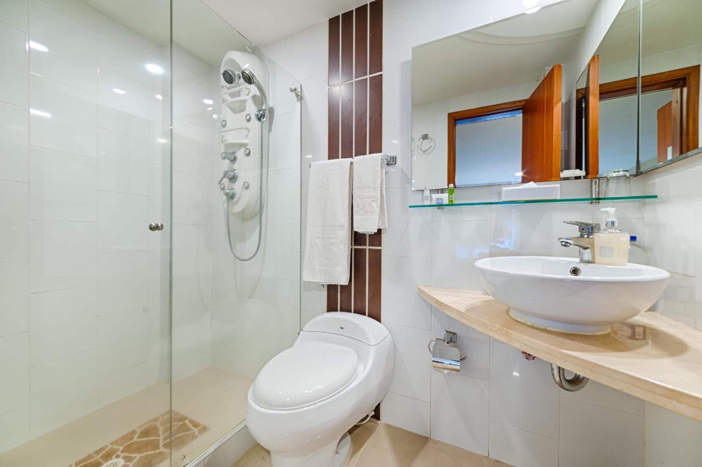 A modern bathroom with a glass-enclosed shower, a white toilet, and a beige vanity with a large sink.