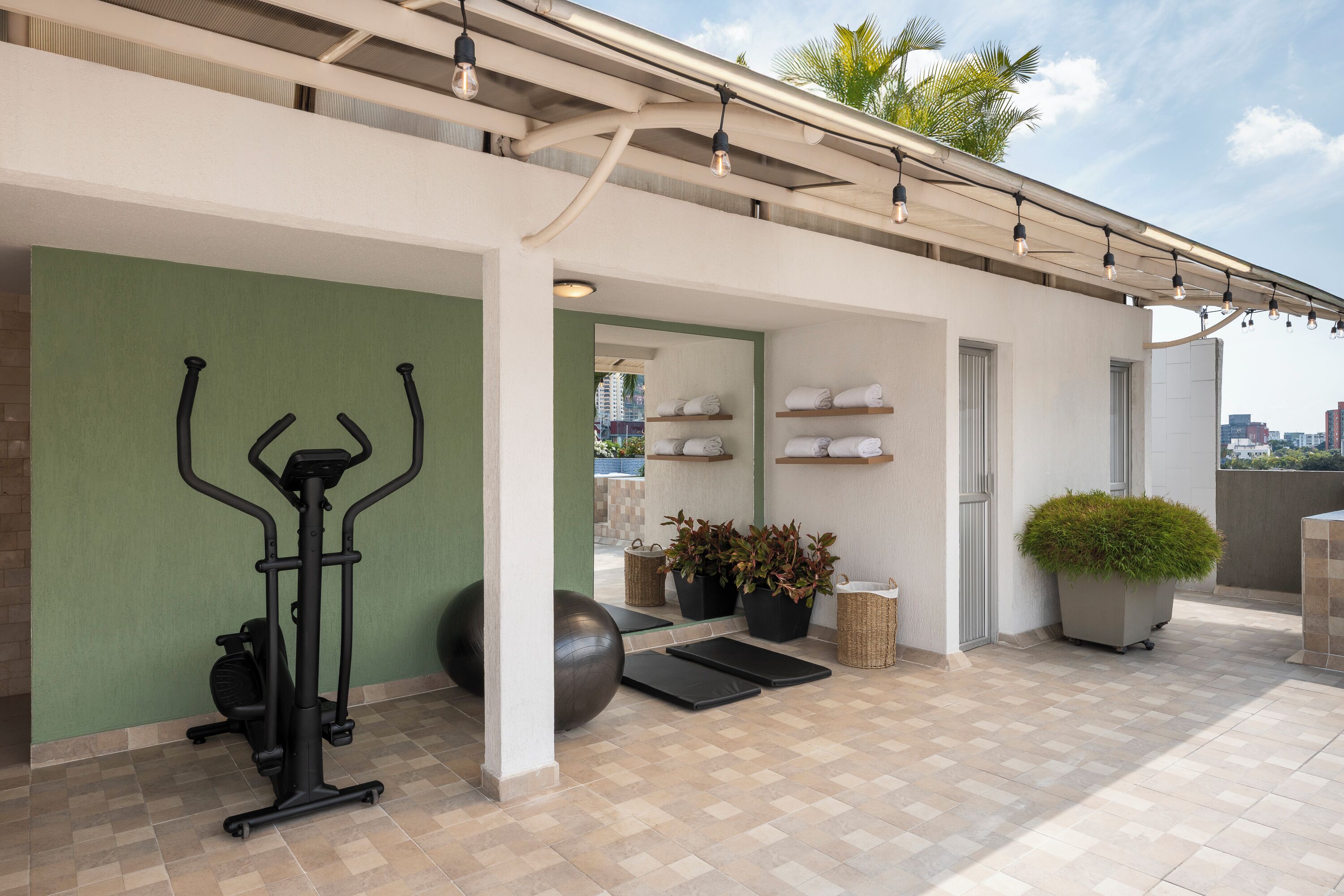 A rooftop gym with exercise equipment, a small seating area, and a view of the city.