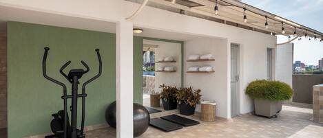 A rooftop gym with exercise equipment, a small seating area, and a view of the city.