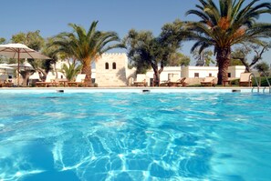 Una piscina azul cristalina con sillas de descanso y palmeras.