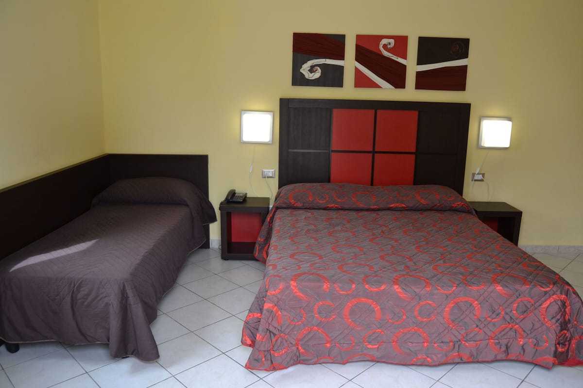 A hotel room with a double bed, a single bed, two bedside tables, and a nightstand.