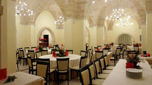 Uma área de refeições com várias mesas redondas e cadeiras, decorada com guardanapos vermelhos e pequenos vasos de plantas.