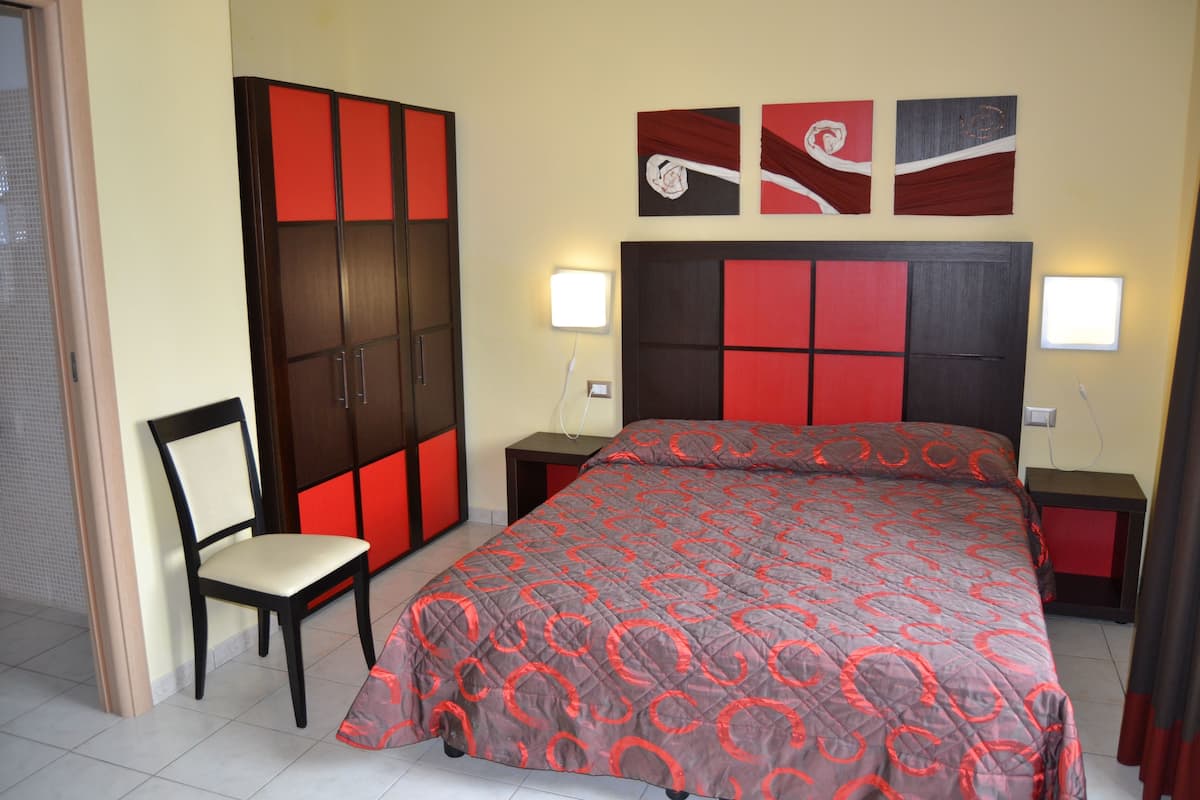 A bedroom with a bed, a chair, a wardrobe, and two bedside tables with lamps.