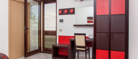 A hotel room with a bed, a desk, a chair, a wardrobe, a television, and a sliding door.