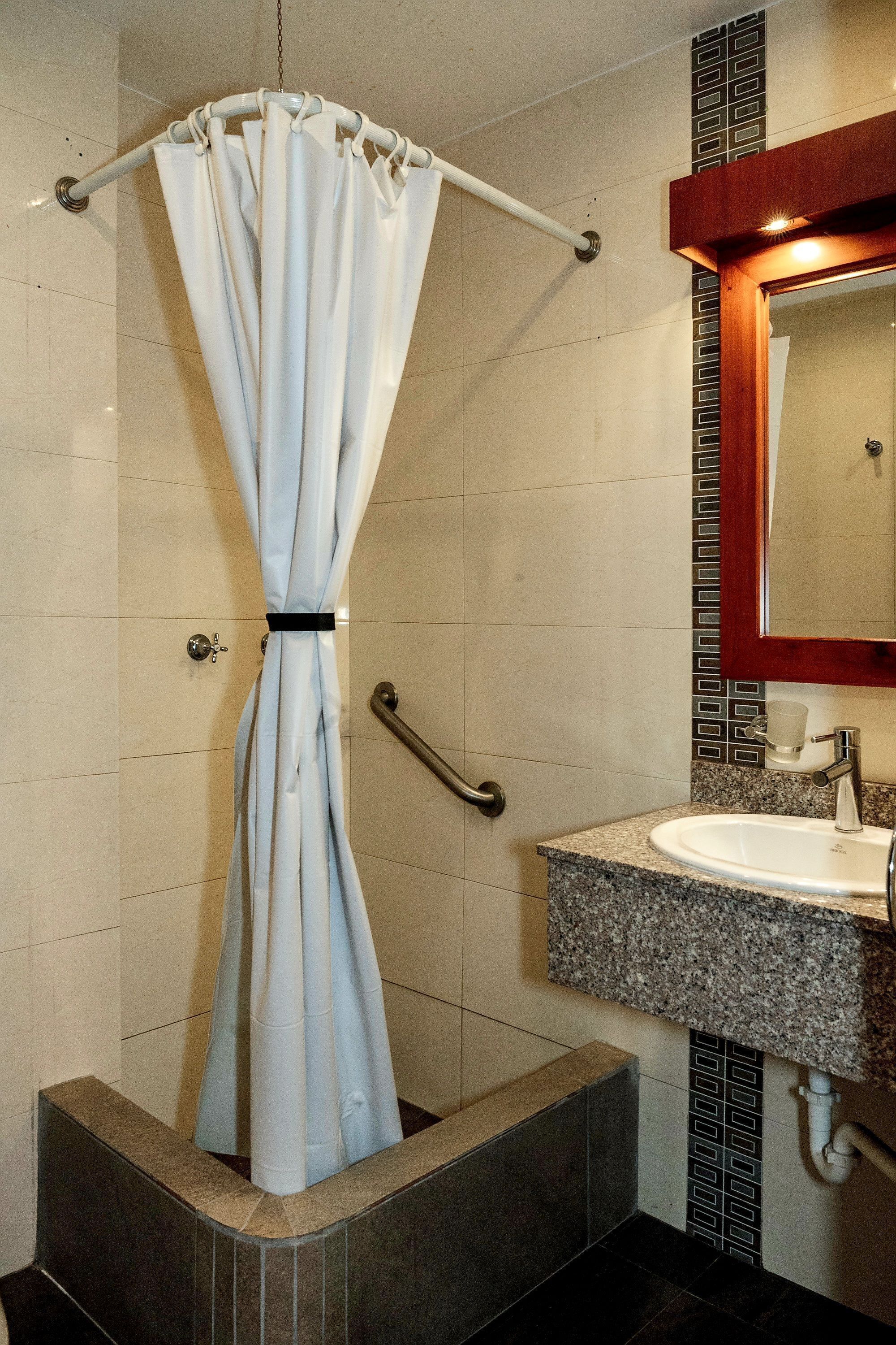 Un baño con cortina de ducha, lavabo con espejo y paredes de azulejos.