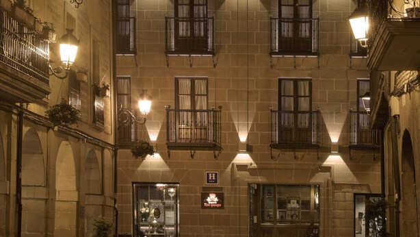 Un bâtiment historique doté de nombreux balcons, de fenêtres illuminées et d’une entrée centrale surmontée d’une enseigne.