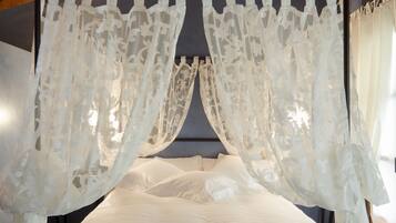 A bed with white bedding and sheer white curtains.
