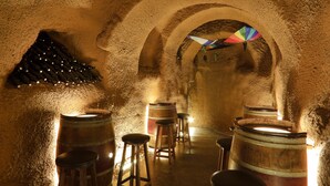Une cave faiblement éclairée, avec des tonneaux en bois et des tabourets disposés en rangée, menant à une porte en arc de cercle.