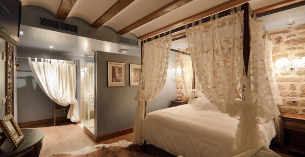 A bedroom with a four-poster bed, a stone wall, and a wooden ceiling.
