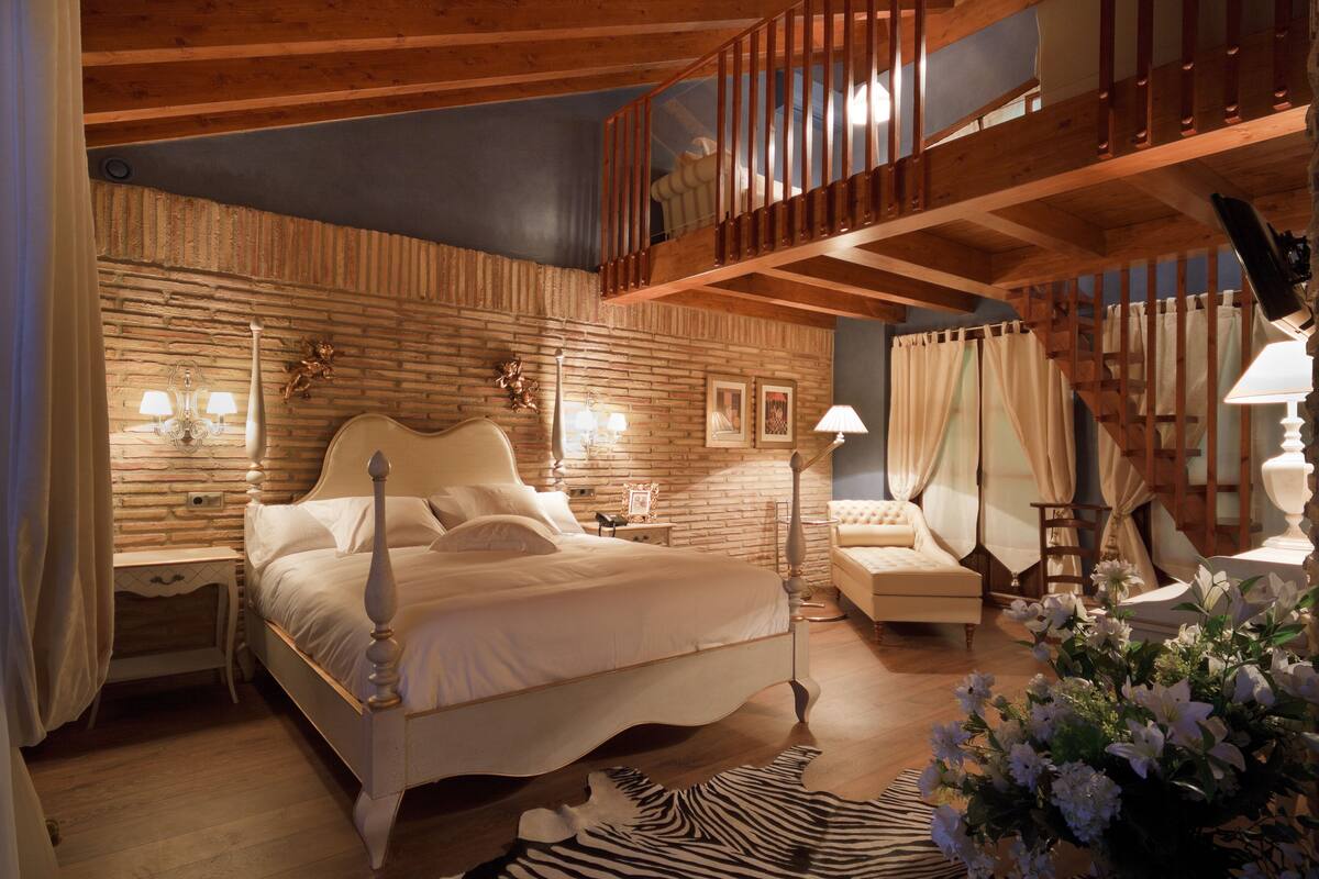Une chambre avec un grand lit, un plafond en bois, un escalier et une vue sur l’extérieur.