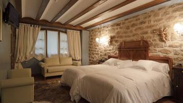 A bedroom with a large bed, a sofa, a chair, a stone wall, and a television.