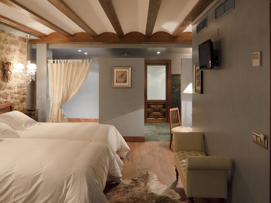 A bedroom with two beds, a wooden headboard, a stone wall, a television, and a door with a geometric design.