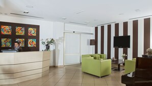 Een receptiegedeelte met een balie, stoelen, een televisie en kleurrijke kunstwerken aan de muur.