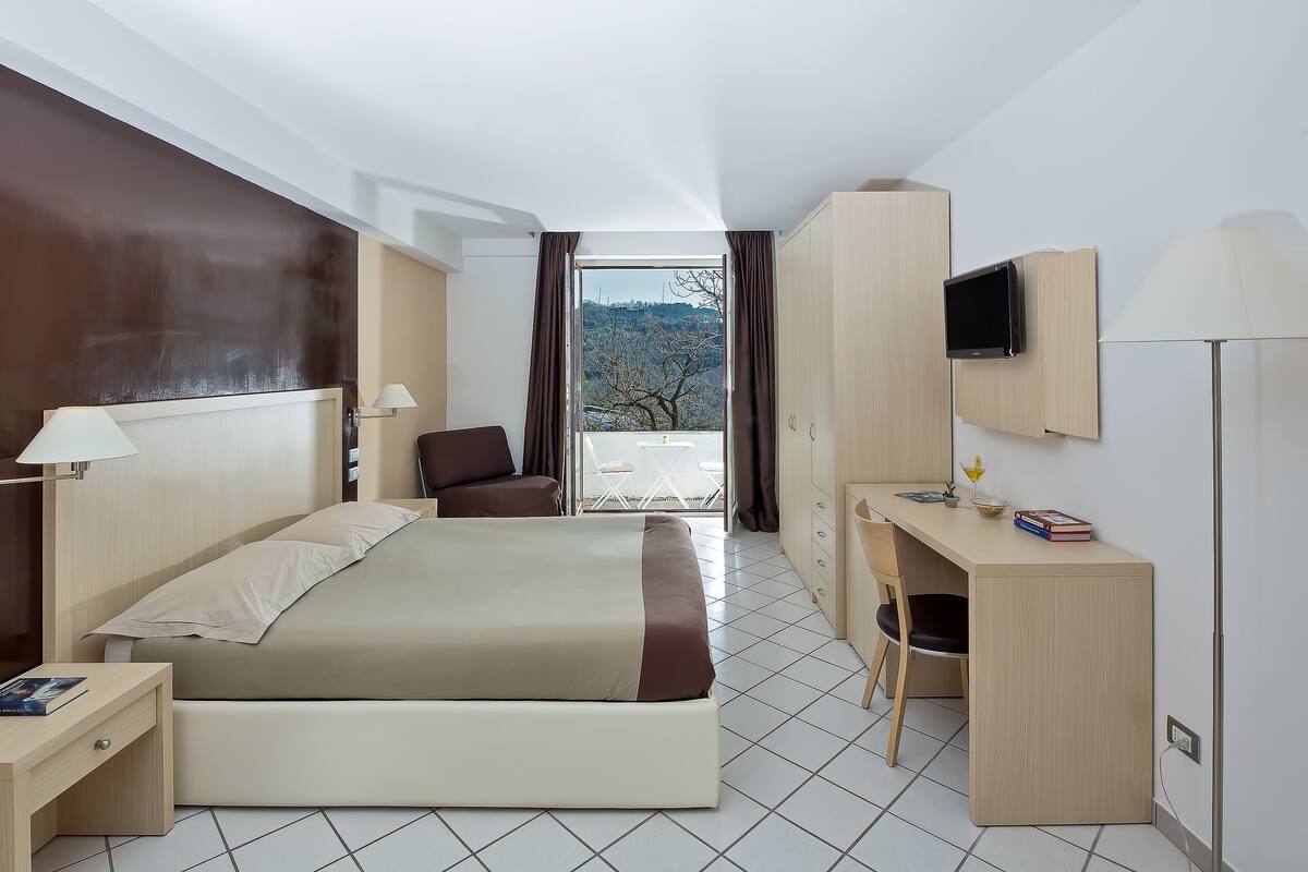 Une chambre d’hôtel moderne équipée d’un lit, d’un bureau, d’une chaise, d’une télévision et offrant une vue sur l’extérieur.