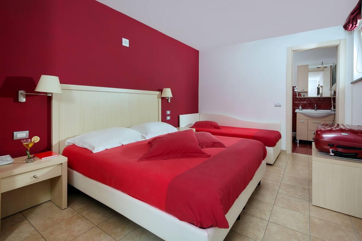 Une chambre d’hôtel avec un grand lit, deux tables de chevet, un bureau et un mur rouge.