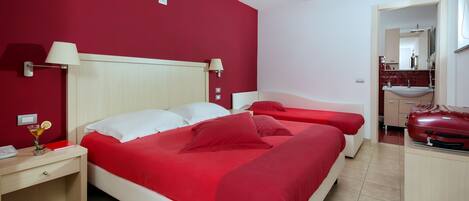 Una habitación de hotel con una cama grande, dos mesitas de noche, un escritorio y una pared roja.