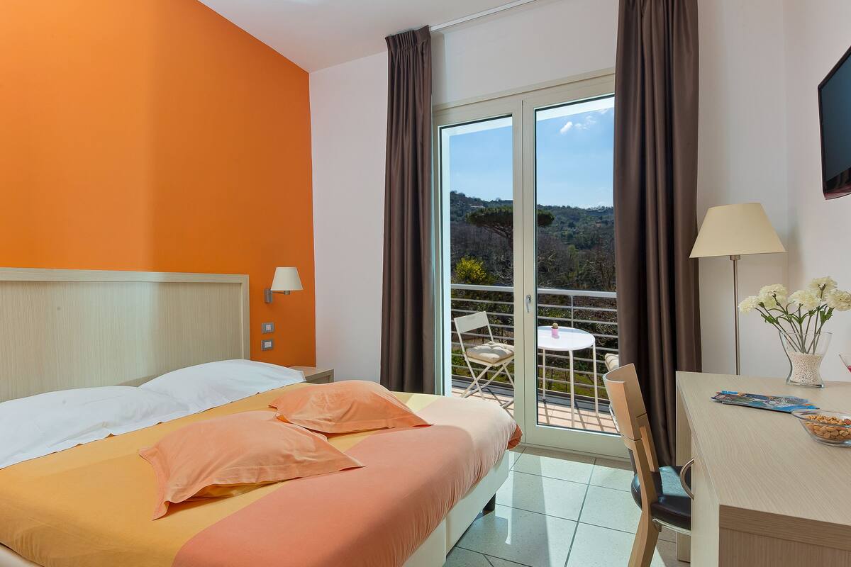Une chambre d’hôtel équipée d’un lit, d’un bureau, d’une chaise, d’une télévision et d’un balcon offrant une vue sur le paysage.