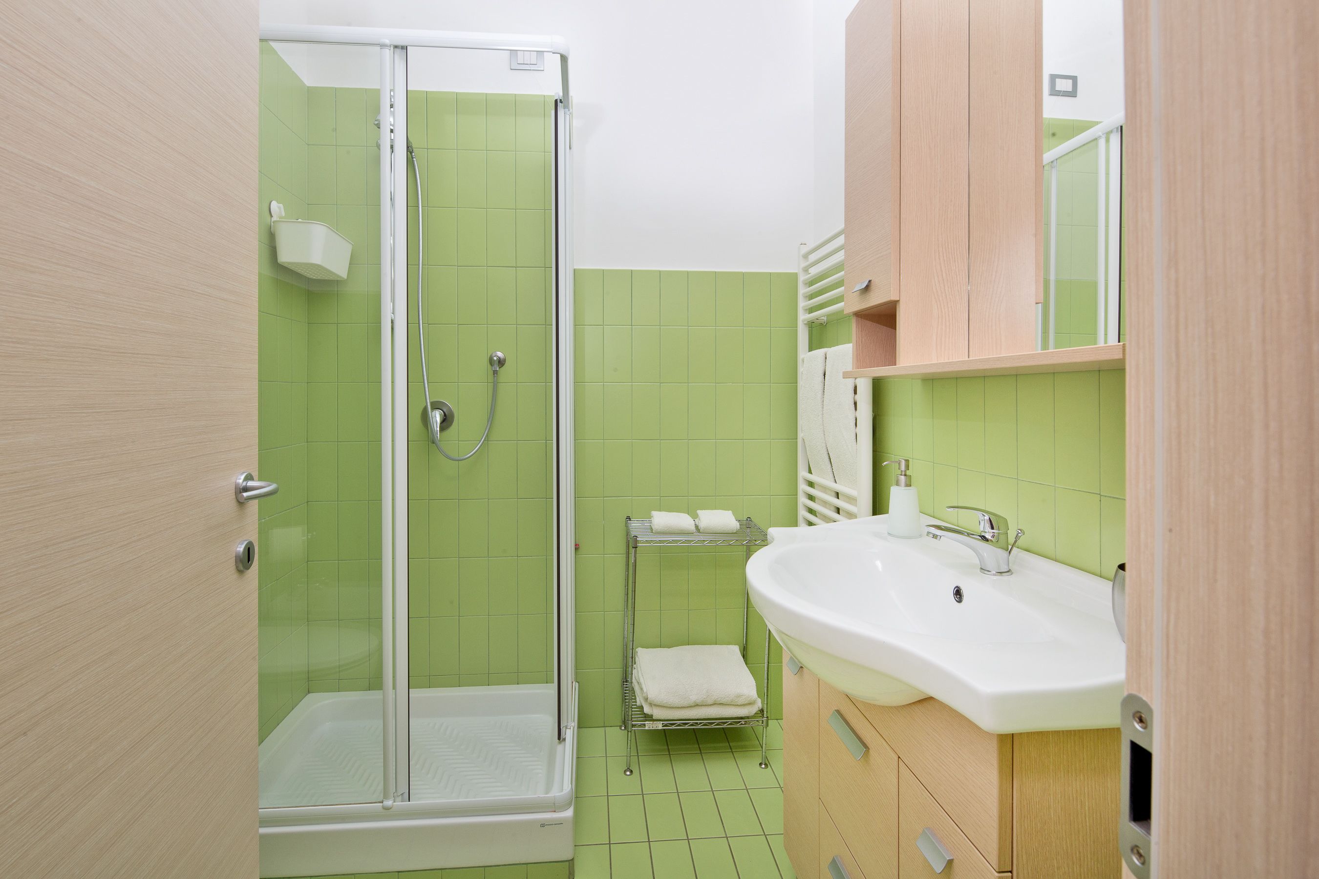A bathroom with a glass-enclosed shower, a sink with a mirror, and a towel rack.