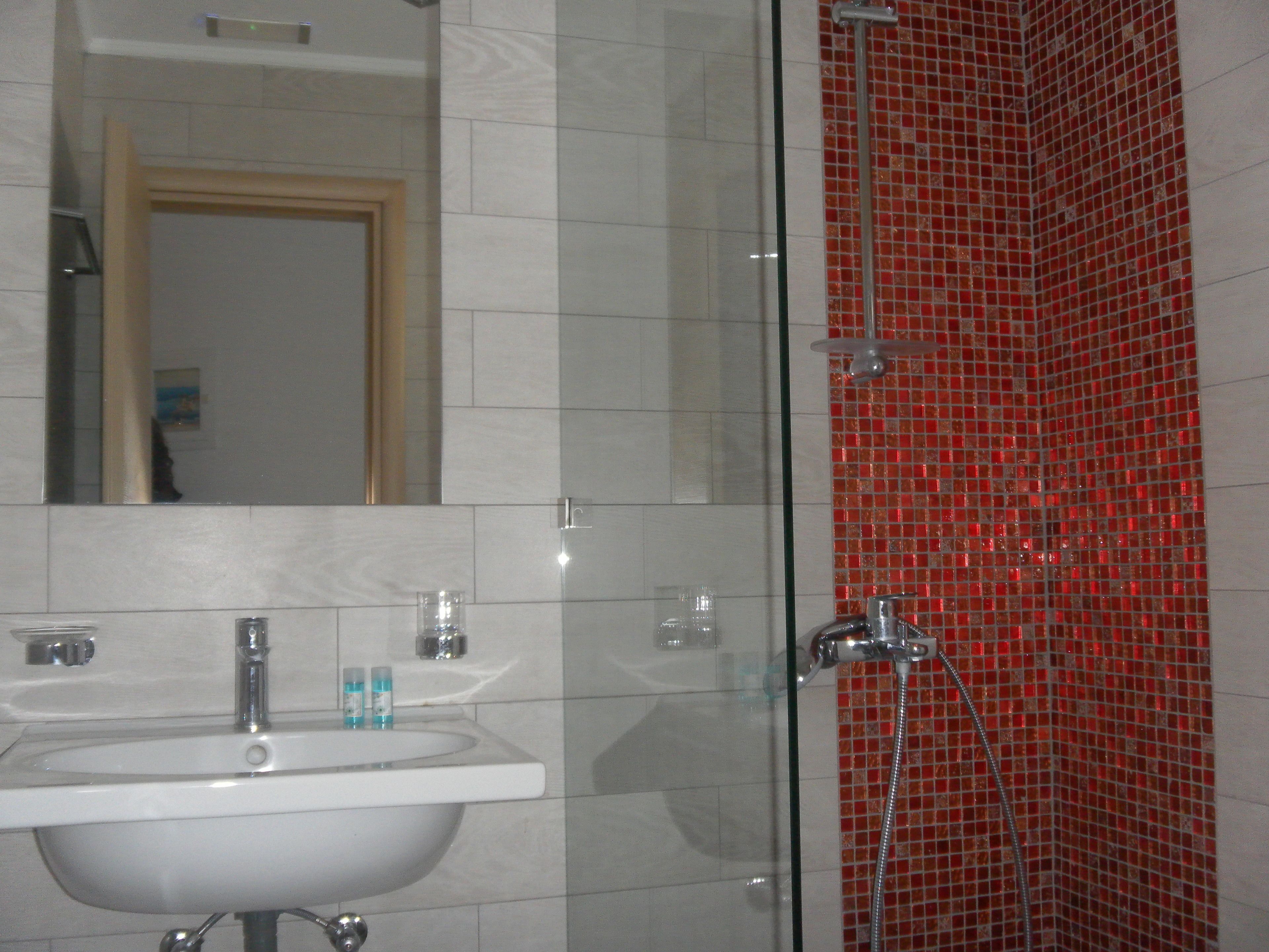 A bathroom with a white sink, a mirror, and a shower with red mosaic tiles.