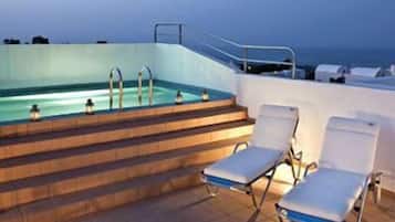 Una piscina con escalones que bajan al agua, rodeada de sillones de descanso y una barandilla.