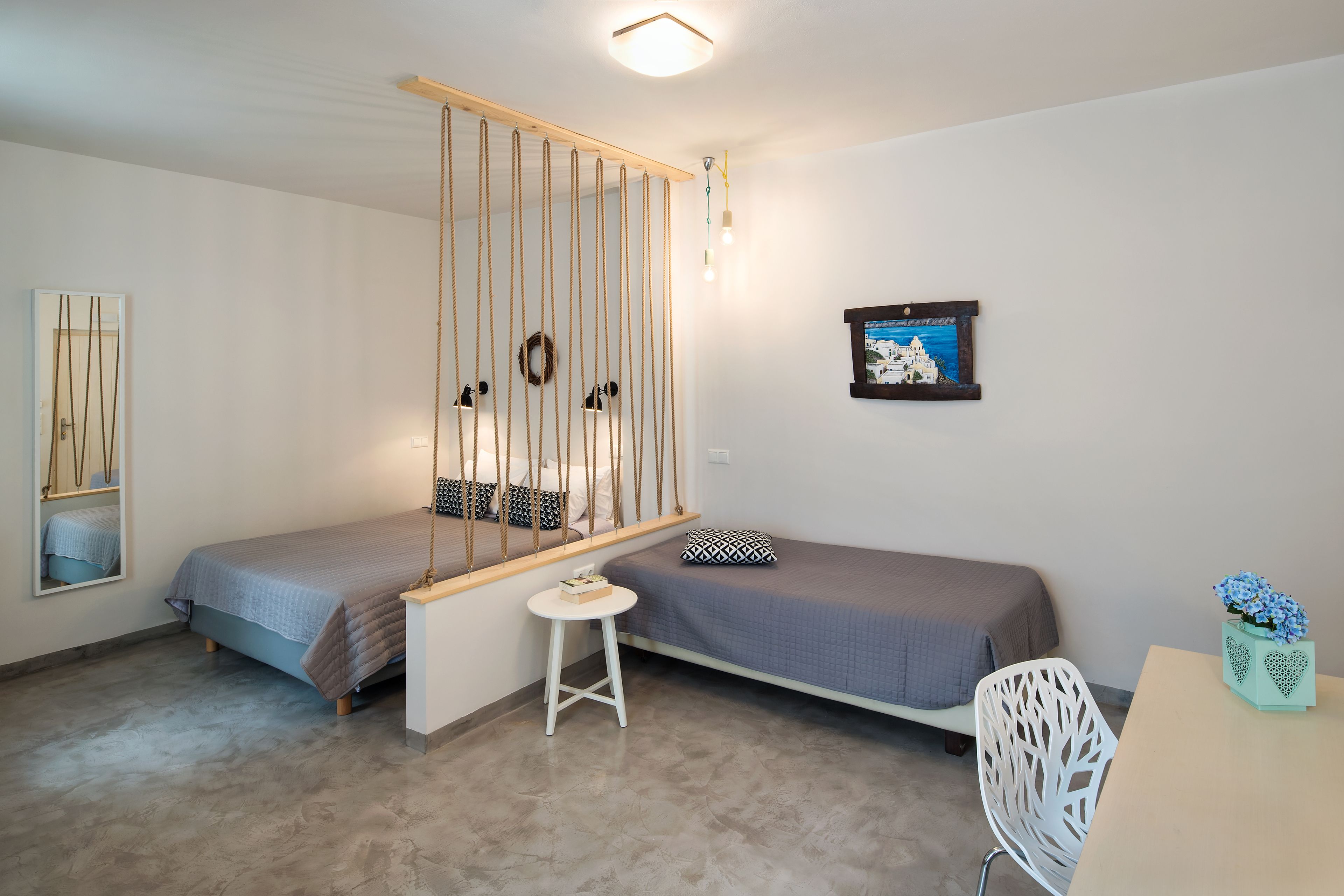 A small, modern room with two single beds, a small table, a chair, and a hanging light fixture.