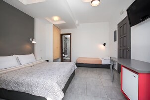 Una habitación de hotel moderna con una cama grande, una cama más pequeña, un escritorio con un armario rojo y blanco, y un televisor montado en la pared.