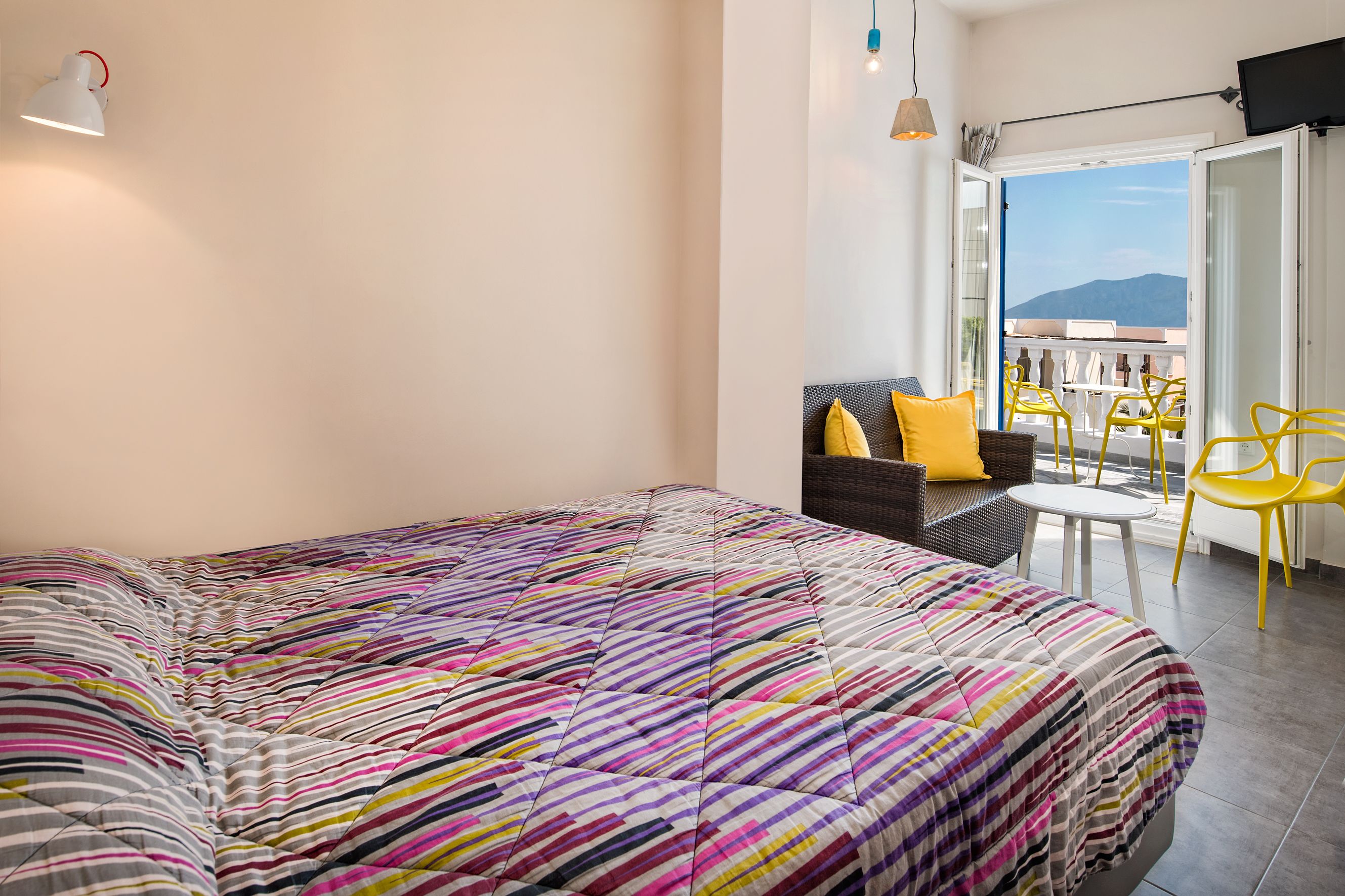 A bedroom with a colorful striped bedspread, a sofa with yellow cushions, a small round table, and yellow chairs.