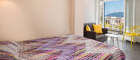 Un dormitorio con una colcha a rayas coloridas, un sofá con cojines amarillos, una mesita redonda y sillas amarillas.