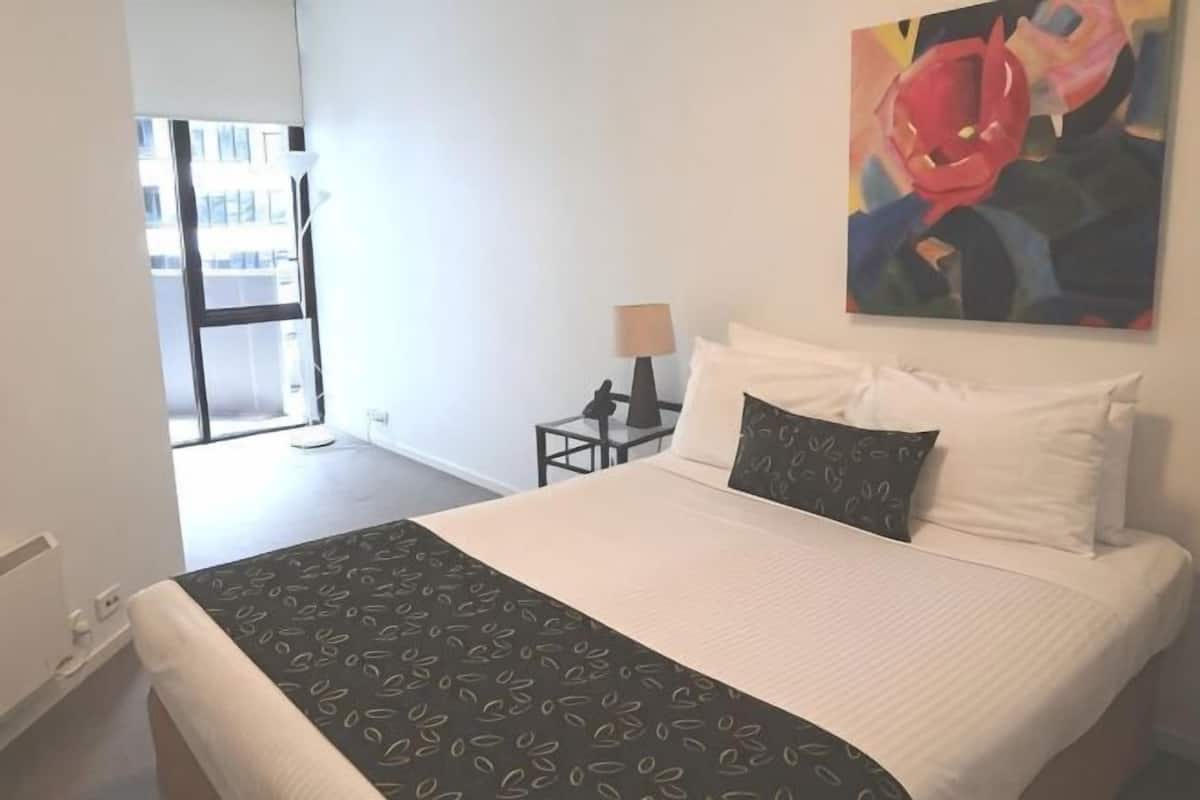 A hotel room with a bed, a nightstand, a lamp, and a painting on the wall.