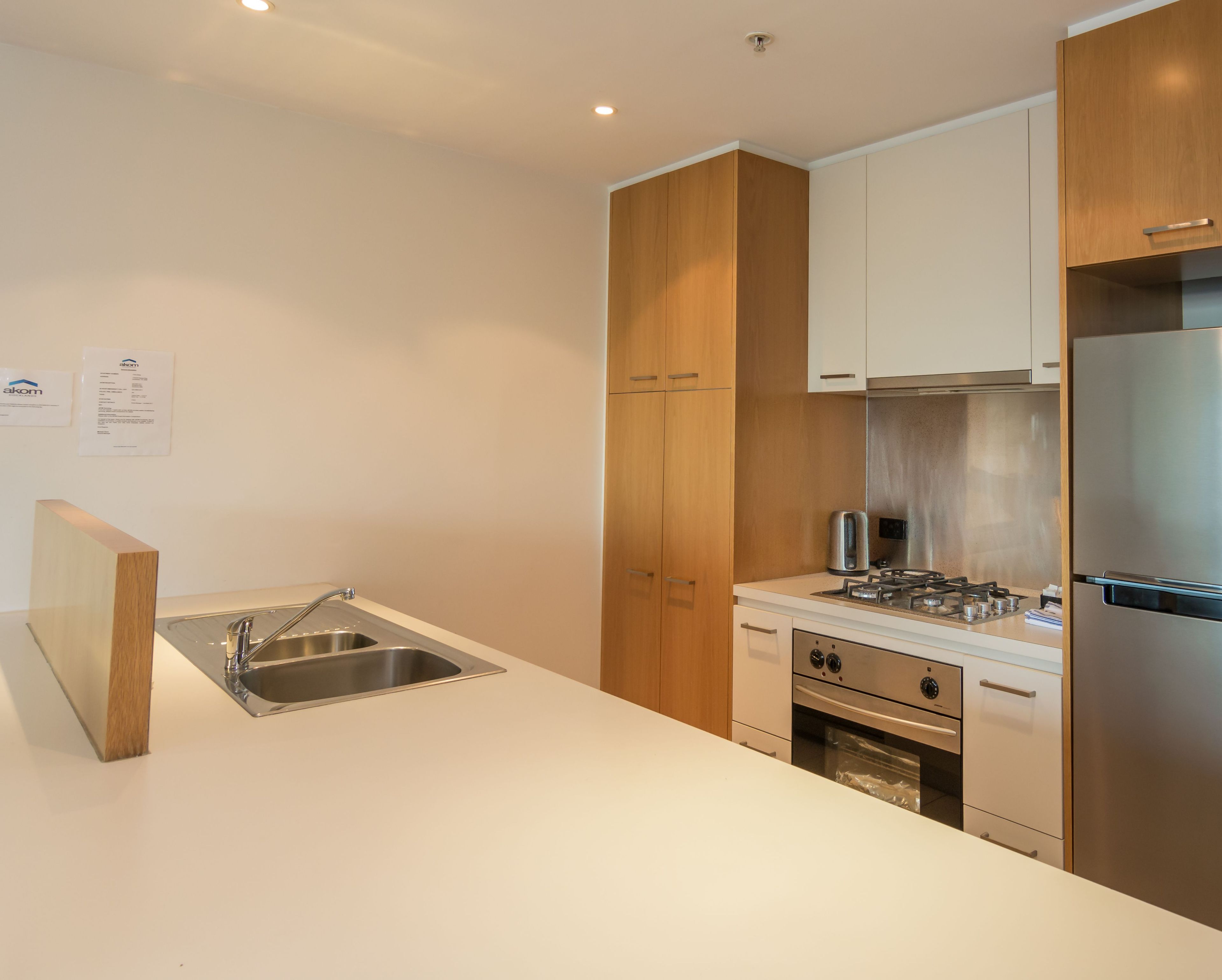 Eine moderne Küche mit einer Edelstahl-Spüle, Holzschränken, einer weißen Arbeitsplatte, einem Gasherd und einem eingebauten Backofen.