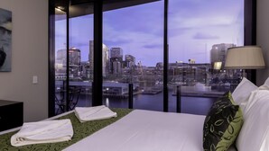 A hotel room with a bed, a view of a city skyline, and a large window. - AKOM AT Docklands (Docklands)