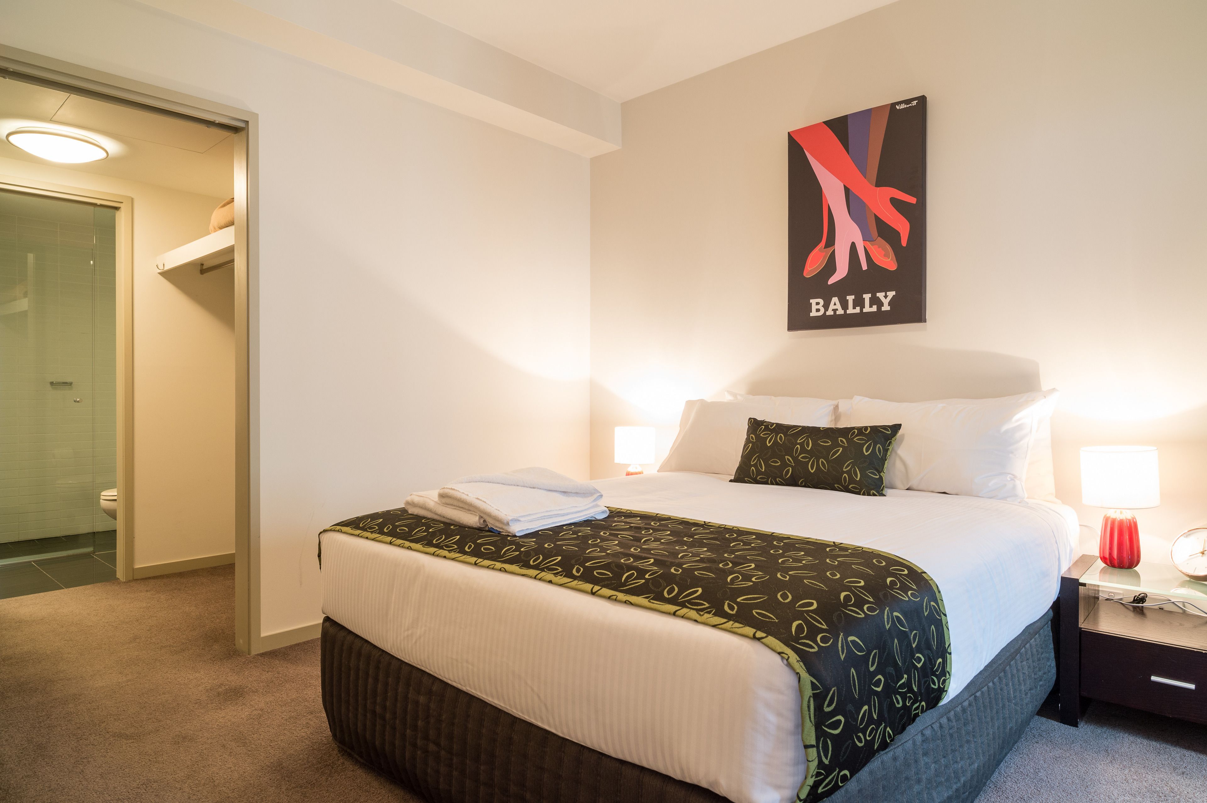 Une chambre d’hôtel avec un lit, une table de chevet, une lampe et une affiche au mur.